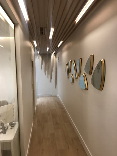 Reforma de Pasillo decorativo en una clínica dental de Madrid, con espejos modernos enmarcados en dorado, techo con diseño lineal e iluminación cálida.